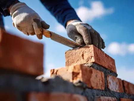 Mason setting brick on mortar while building a backyard outdoor fireplace